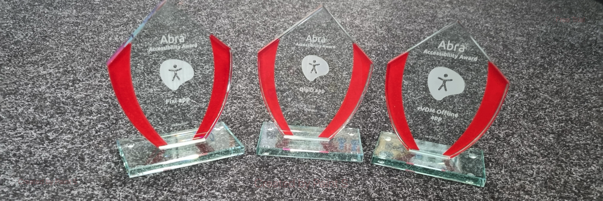 Three Abra Accessibility Awards, they are made of glass and have a red accent color